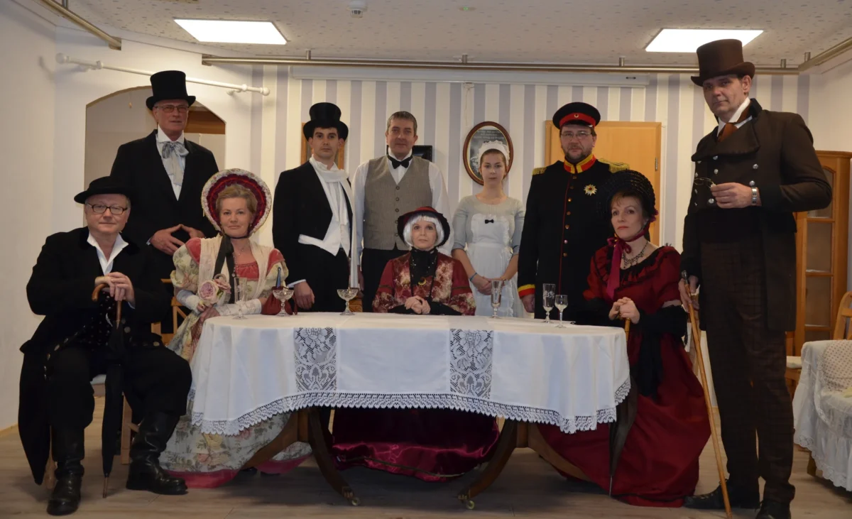 Das Ensemble von „Da kahle Krempling“ 2019 in Kostümen um eine weiß gedeckte Tafel
