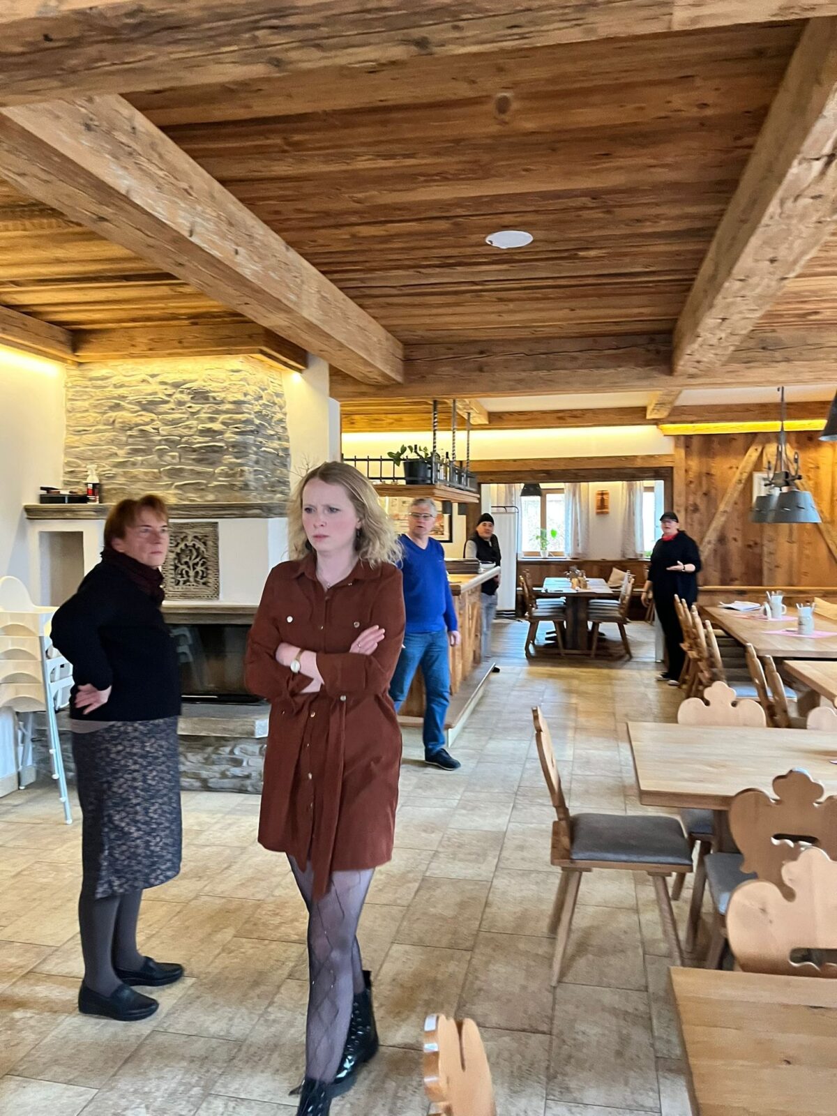 Probe in der leeren Gaststube mit Steinkamin: Darstellerin im braunen Kleid mit verschränkten Armen, weitere Spieler dahinter
