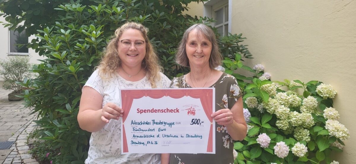 Spendenübergabe: zwei Frauen halten in einem Innenhof vor Hortensien einen großen Spendenscheck der Theatergruppe über 500 Euro