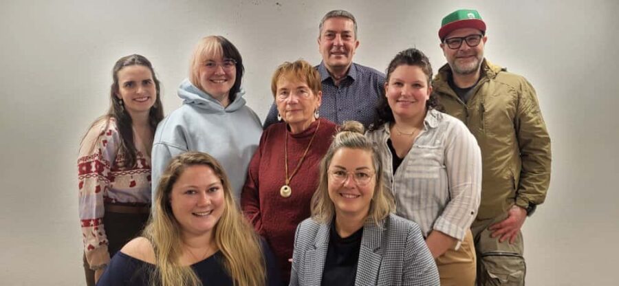 Gruppenfoto der Vorstandschaft: acht Personen in Freizeitkleidung, zwei vorn sitzend, sechs dahinter stehend vor heller Wand